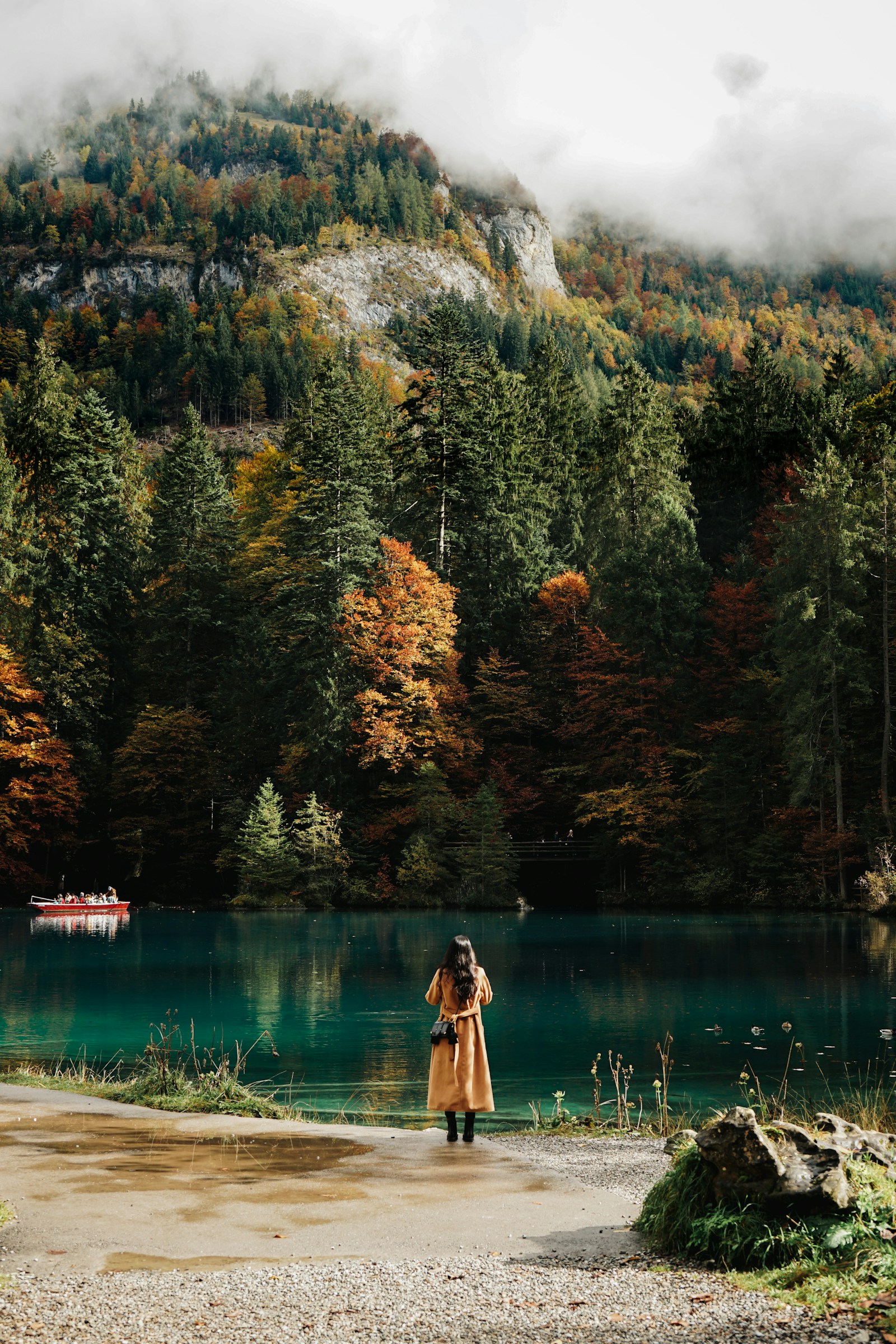A visitor by the turquoise Blausee among autumn forest, red boat behind